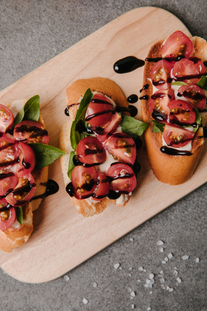 top view of delicious bruschetta with tomatoes and balsamic on wooden board on greyの写真素材