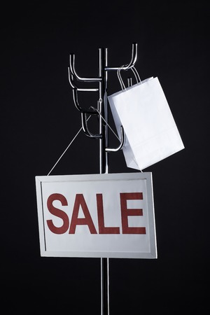 sale signboard and paper bag on coat rack isolated on blackの写真素材