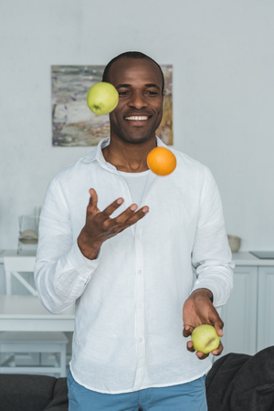 handsome african american man juggling with fruits at homeの写真素材