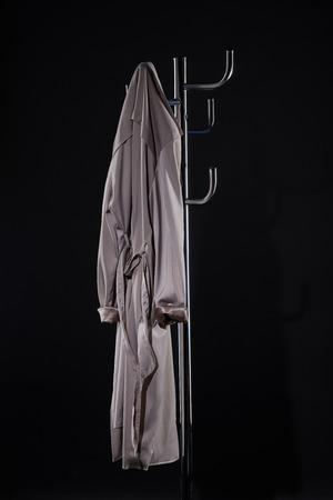 trench coat hanging on coat rack isolated on blackの写真素材