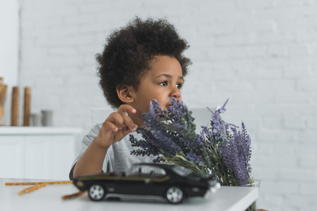 adorable african american boy touching violet flowers and looking away at homeの写真素材