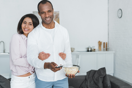 african american girlfriend hugging boyfriend with popcorn at homeの写真素材