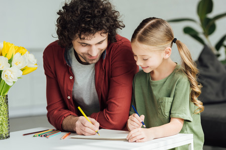 happy father and little daughter drawing with colored pencils at homeの写真素材