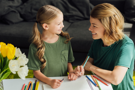 happy mother and daughter drawing together and smiling each other at homeの写真素材