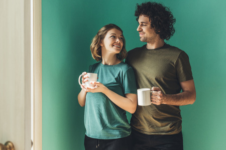 happy couple in t-shirts holding cups and smiling each other