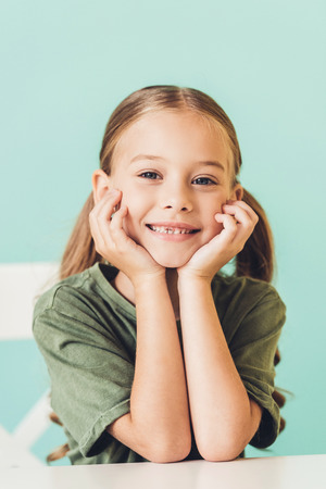 portrait of adorable little child sitting at table and smiling at cameraの写真素材