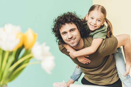 selective focus of father piggybacking adorable happy daughter and smiling at cameraの写真素材
