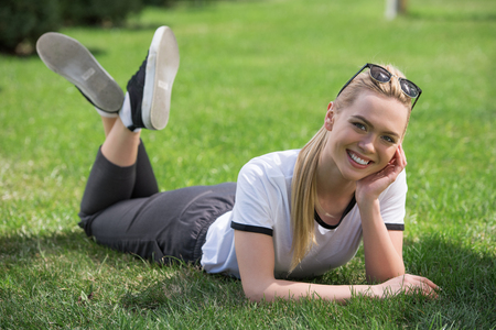 beautiful young blonde woman lying on green grass and smiling at cameraの写真素材