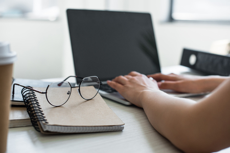 close-up view of spectacles on notepad and person using laptop behindの写真素材