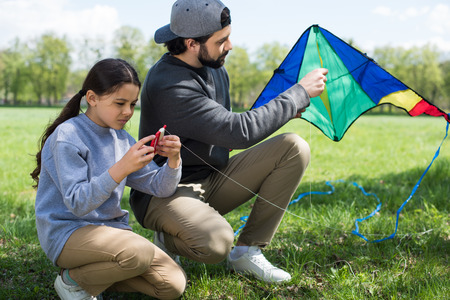 father and daughter sitting with kite on meadow in park