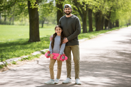 smiling father and daughter holding skateboard in parkの写真素材