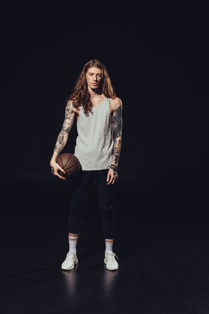 tattooed man standing with basketball ball, on blackの写真素材
