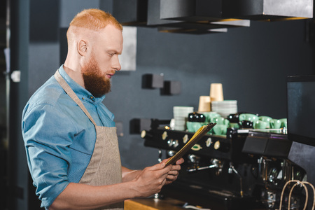 side view of young male barista looking at menu in coffee shopの写真素材