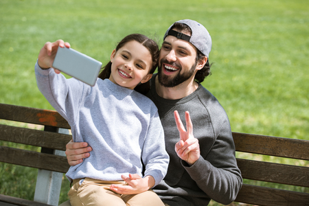 daughter taking selfie with father doing peace gesture in parkの写真素材