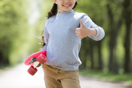 cropped image of child with penny board doing thumb up gestureの写真素材