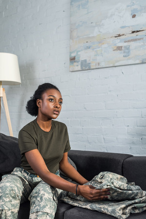 Female army soldier folding camouflage clothes on sofaの写真素材