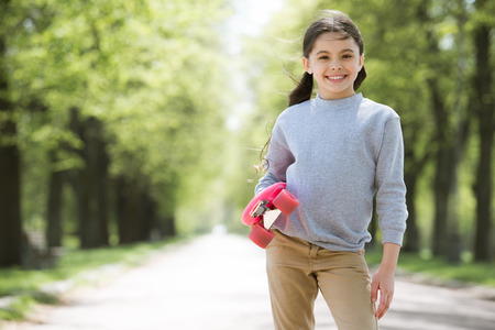 little smiling child holding penny board in parkの写真素材