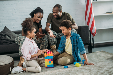 African american man and woman soldiers looking at their children playing with cubesの写真素材