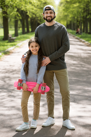 daughter with skateboard and father on path in parkの写真素材