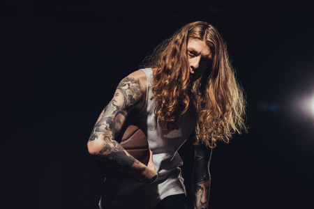 tattooed man with long hair playing basketball, isolated on blackの写真素材