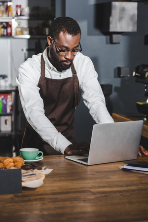 young african american barista using laptop while working in cafeの写真素材