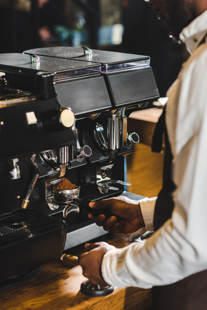 cropped shot of african american barista in apron preparing coffee at coffee machineの写真素材