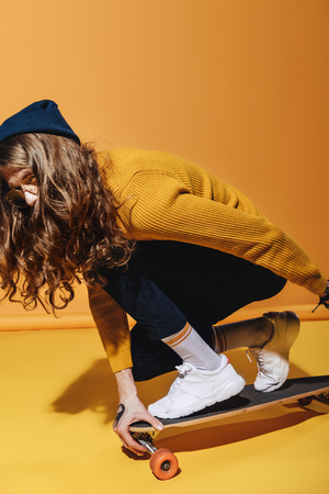 stylish man with long hair sitting on longboard, on yellowの写真素材