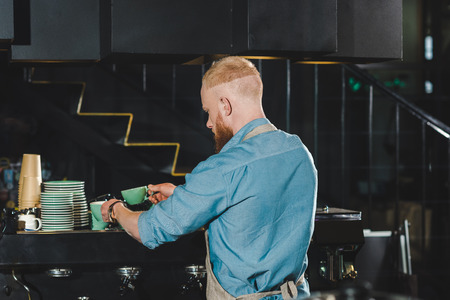 rear view of young male barista pouring coffee into mug