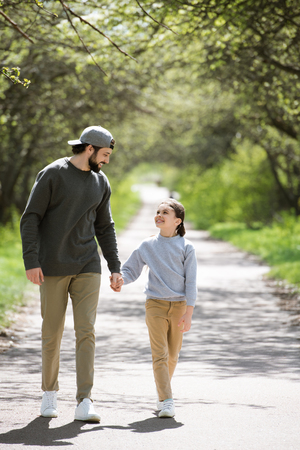 smiling father and daughter walking and holding hands in parkの写真素材