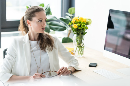 businesswoman looking at computer screen at workplace with bouquet of flowers in vase in officeの写真素材