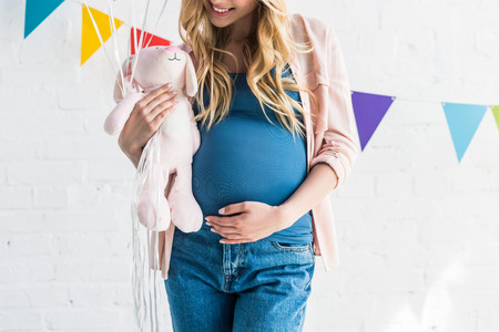 cropped image of pregnant woman touching belly and holding rabbit toy at baby-partyの写真素材