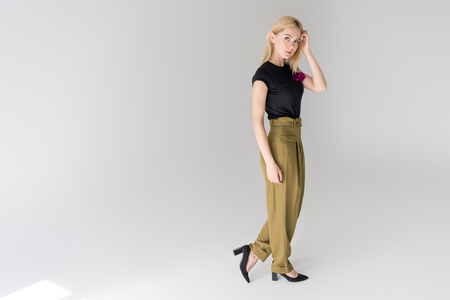 full length view of stylish young woman looking at camera and posing on greyの写真素材