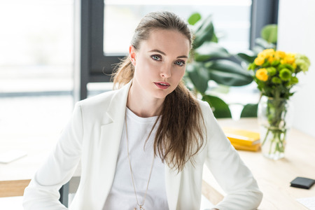 portrait of beautiful businesswoman in white suit looking at camera in office