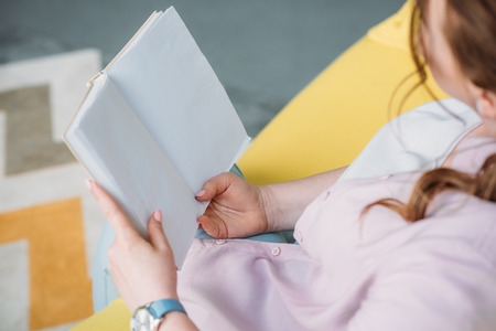 cropped image of woman reading book on sofa at home