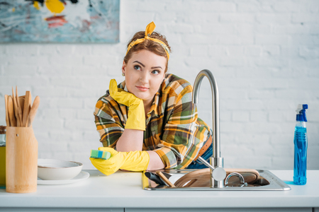 beautiful woman leaning on kitchen counter and holding washing spongeの写真素材