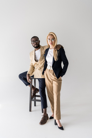 full length view of stylish young multiethnic couple in spectacles looking at camera isolated on greyの写真素材