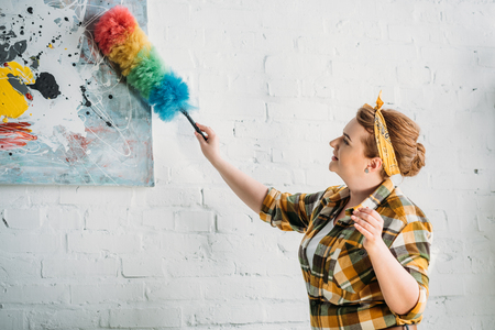 beautiful woman dusting paint on wall at homeの写真素材