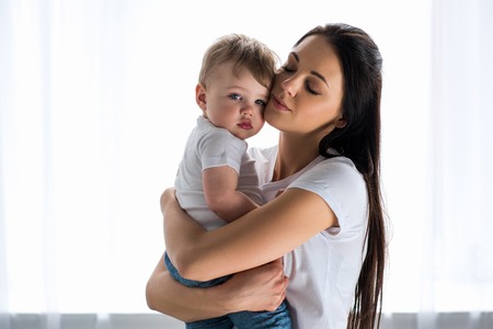 portrait of tender mother holding cute baby in hands at homeの写真素材