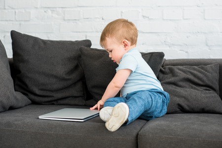 side view of little baby boy with laptop on sofa at homeの写真素材