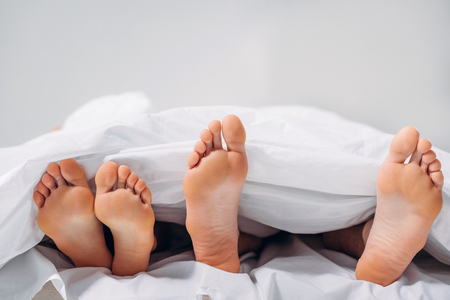 cropped shot of female and male legs in bedの写真素材