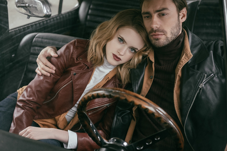 beautiful stylish young couple in leather jackets embracing in retro carの写真素材