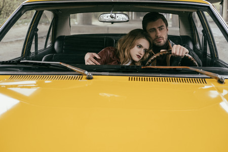 handsome young man driving car and embracing beautiful pensive girlfriend