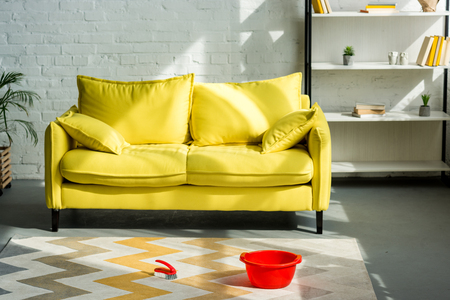 red bucket and cleaning brush on carpet on floor, yellow sofa in living roomの写真素材