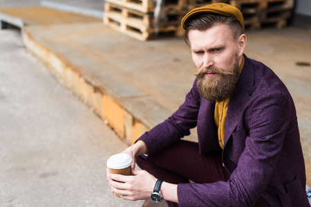 Handsome businessman in vintage style clothes sitting on street with paper cup in handsの写真素材