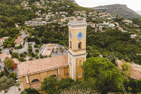 aerial view of church with bell tower and clock at small european town on hills, Eze, France