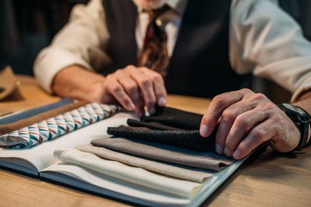 cropped shot of tailor working with cloth samples at sewing workshop in late eveningの写真素材
