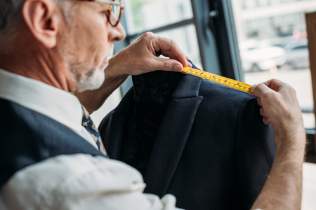 side view of senior tailor measuring jacket with tape measure at sewing workshopの写真素材