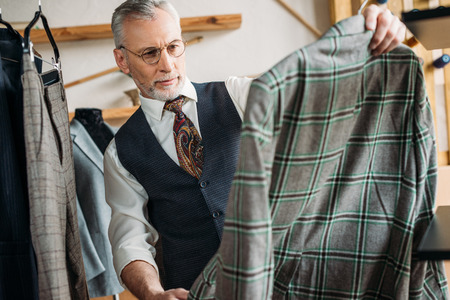serious mature tailor examining clothes at sewing workshopの写真素材