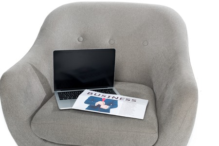 laptop with blank screen and business newspaper on grey armchairの写真素材