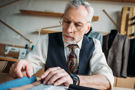 handsome mature tailor looking at cloth samples at sewing workshopの写真素材